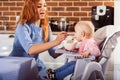 Little baby girl sits in high chair and feeding with spoon her beautiful mother Royalty Free Stock Photo
