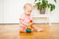 Little baby girl sitting on the floor, crawling and playing with brightly colored educational toys