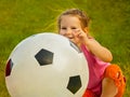 Little baby girl sitting with a huge ball of football colors. Royalty Free Stock Photo
