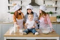 Little baby girl is sitting on the wooden table at kitchen while her mother, aunt and grandmother read the book with Royalty Free Stock Photo