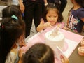 Little baby girl sneakily reaching her hand out to a birthday cake in front of her, as it is so irresistibly attracted to her