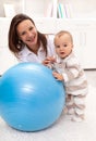 Little baby girl stands by a large exercise ball