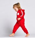 Little baby girl toddler walking making first steps in red cloth on grey