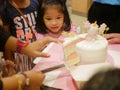 Little baby girl watching a birthday cake in front of her being cut / slices, as it is so irresistibly attracted to her
