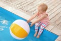 Little baby reaching for inflatable ball at swimming pool. Dangerous situation