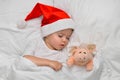 Little baby sleeping on white linen in the Santa hat with his toy pig, wich is the symbol of the year 2019.