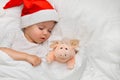 Little baby sleeping on white linen in the Santa hat with his toy pig, wich is the symbol of the year 2019. Royalty Free Stock Photo