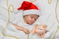 Little baby sleeping on white linen in the Santa hat with his toy pig, wich is the symbol of the year 2019. Royalty Free Stock Photo