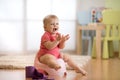 Little baby girl claps sitting on chamberpot in nursery room Royalty Free Stock Photo