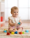 Adorable baby playing with colorful toy pyramid sitting on carpet in white sunny bedroom. Toys for little kids. Child Royalty Free Stock Photo
