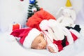 Little baby wearing Santa Claus costume sleep on white fur carpet with red gift bag and doll Royalty Free Stock Photo