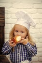 Little baker. Child eating bread bun on white brick wall Royalty Free Stock Photo