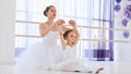 Little ballerina in white tutu is stretching on ballet lesson with teacher.