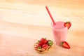 Little basket full of strawberries is standing on a desk next to transparent glass of delish coral smoothie with a red straw. Royalty Free Stock Photo