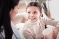 Little beaming schoolgirl feeling delighted enjoying tea break with mother