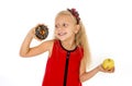 Little beautiful blond child choosing dessert holding unhealthy chocolate donut and apple fruit Royalty Free Stock Photo