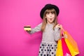 Little beautiful child girl in black hat holding shopping bags and credit card isolated on pink Royalty Free Stock Photo