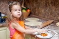 Little beautiful cute girl in orange apron smiling and making homemade pizza, roll the dough at home kitchen. Concept happy family Royalty Free Stock Photo