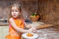 Little beautiful cute girl in orange apron smiling and making homemade pizza, roll the dough at home kitchen. Concept happy family Royalty Free Stock Photo