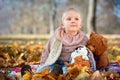 Little beautiful dreamy caucasian girl with earrings in autumn park sits in golden autumn leaves with with soft toys Royalty Free Stock Photo