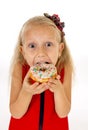 Little beautiful female child with long blonde hair and red dress eating sugar donut with toppings delighted and happy Royalty Free Stock Photo