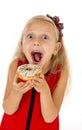 Little beautiful female child with long blonde hair and red dress eating sugar donut with toppings delighted and happy