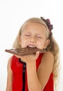 Little beautiful female child in red dress holding happy delicious chocolate bar in her hands eating delighted Royalty Free Stock Photo