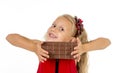 Little beautiful female child in red dress holding happy delicious chocolate bar in her hands eating delighted Royalty Free Stock Photo