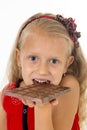 Little beautiful female child in red dress holding happy delicious chocolate bar in her hands eating delighted Royalty Free Stock Photo