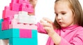 Little beautiful focused schoolgirl sits at the table playing with colorful plastic construction blocks on white background.