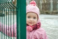 Little beautiful girl baby behind the fence, grid locked in a cap and a jacket with sad emotion on his face