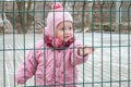 Little beautiful girl baby behind the fence, grid locked in a cap and a jacket with sad emotion on his face
