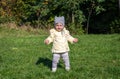 Little beautiful girl baby coat, hat and jeans playing in the park walking on green grass doing their first steps smiling and enjo Royalty Free Stock Photo