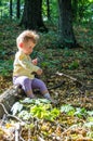 Little beautiful girl baby playing with a stick sitting on a log