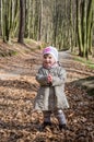 Little beautiful girl in a baby raincoat, hat and scarf is played in spring forest dry leaf litter throwing their smiles in a good