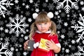 Little beautiful girl in a Christmas Santa suit, with fur balls on her head, holds gifts in her hands and rejoices Royalty Free Stock Photo