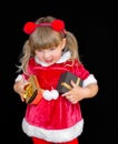 Little beautiful girl in a Christmas Santa suit, with fur balls on her head, holds gifts in her hands and rejoices. Royalty Free Stock Photo