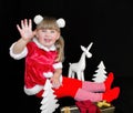 Little beautiful girl in a Christmas Santa suit, with fur balls on her head, holds gifts in her hands and rejoices. Royalty Free Stock Photo