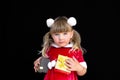 Little beautiful girl in a Christmas Santa suit, with fur balls on her head, holds gifts in her hands and rejoices. Royalty Free Stock Photo