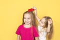 Little beautiful Girl combing hair with a big comb her older sister isolated on yellow background Royalty Free Stock Photo