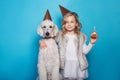 Little beautiful girl with dog celebrate birthday. Friendship. Love. Cake with candle. Studio portrait over blue background Royalty Free Stock Photo