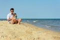 A father with a little daughter sits on the beach at the background of the sea Royalty Free Stock Photo