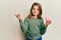 Little beautiful girl holding tasty colorful doughnut smiling happy pointing with hand and finger to the side Royalty Free Stock Photo