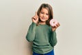 Little beautiful girl holding tasty colorful doughnut smiling with an idea or question pointing finger with happy face, number one Royalty Free Stock Photo