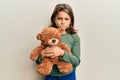 Little beautiful girl hugging teddy bear skeptic and nervous, frowning upset because of problem Royalty Free Stock Photo