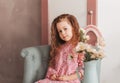 Little beautiful girl with long hair in a pink dress sits in a chair in the children`s room and poses for the camera.Little lady. Royalty Free Stock Photo