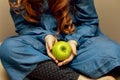 little beautiful girl with long red curly hair in a blue dress sits and holds a green apple in her hands, close-up, baby Royalty Free Stock Photo