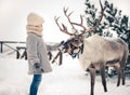 Little girl playing with a deer in the winter snow forest. Christmas fairytale Royalty Free Stock Photo