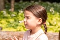 Little beautiful girl with a ponytail squinting looking up while standing on the shore of a pond