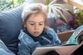 Little girl is reading a book in the living room on the couch Royalty Free Stock Photo